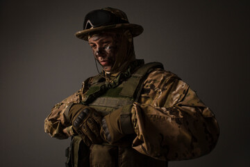 Obraz premium A close-up shot of a military man in a uniform in a hat with goggles giving orders on the grey background. Portrait of the soldier . Calm warrior. Army. Commando. Call of duty.