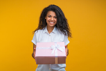 Obraz premium Portrait of attractive smiling stylish young woman posing with decorated gift box in hands, isolated over bright colored yellow background