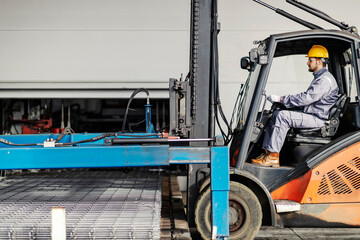 A forklift driver at steel factory transporting iron construction and armature.