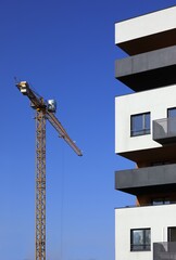 Fototapeta na wymiar Dźwig budowlany na tle błękitnego nieba - budowa domu. Konstrukcje budowalne. Plac budowy osiedla mieszkaniowego.