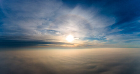Aerial view of bright yellow sunset over white dense clouds with blue sky overhead