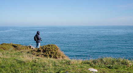 Coastal landscape with calm sea and man in dark coat with hood and camera. Copy space.