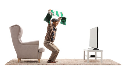 Full length profile shot of an elderly man with a football scarf cheering in front of tv