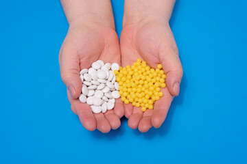 Vitamins in the hands of an adult: white tablets and yellow capsules on a blue background, central...
