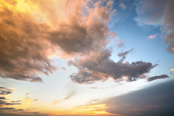 Dramatic sunset landscape picture with puffy clouds lit by orange setting sun and blue sky