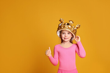 Cute girl in inflatable crown on yellow background, space for text. Little princess