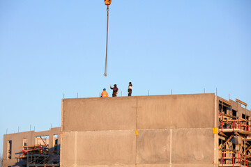 Pracownicy budowani podczas budowy domu na tle niebieskiego wieczornego nieba z dźwigiem budowlanym. - obrazy, fototapety, plakaty