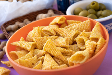Detailed closeup to a bowl with cone-shaped baked corn snacks, isolated on yellow background.