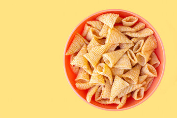 Top view of a bowl with conical shaped baked corn snacks, isolated on yellow background.