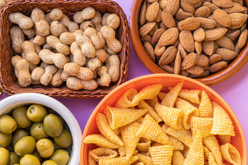Top view of an assortment of appetizers, with peanuts, almonds, anchovy stuffed olives and baked corn snacks. Snack concept.
