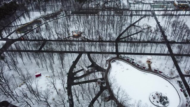 Aerial winter day view in Kharkiv city center Park of Maxim Gorky. White frozen winter lake, bare trees and walking paths around attractions recreation area. Fly forward