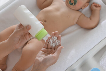 Mother with dusting powder near her baby at home, above view