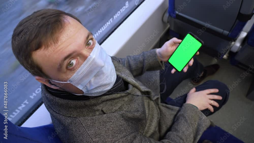 Poster man looks to camera with smart phone with green screen and browsing online in train. mock up for wat