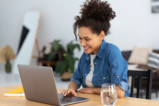 Student studying, distance learning, online education. Portrait of smiling young female freelancer working sitting in co-working or modern office or home. African American woman using laptop computer