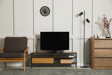 Elegant room interior with modern TV on stand, armchair and wooden chest of drawers