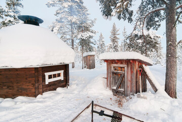 Small wooden huts, and an octagonal wooden building in a clearing in snow covered woods in...