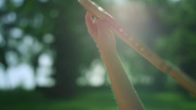 Closeup hand holding wooden badminton racket in golden sunlight in park.