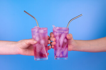 Female hands with pink cold refreshing cocktails in glasses on blue background. Summer drink party...