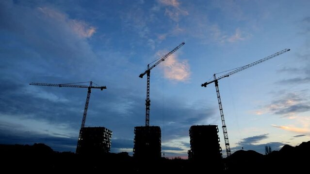 Construction site with black silhouette crane on the background blue sky, three buildings