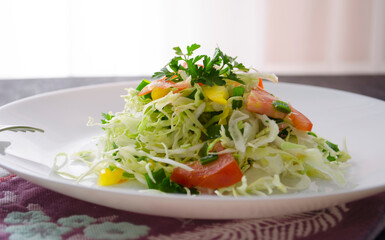 Fresh young cabbage salad on a wooden table. Peppers, tomatoes for the brightness of taste. Seasoning: sunflower oil, salt and black pepper.
