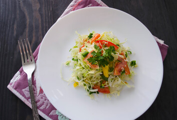 Fresh young cabbage salad on a wooden table. Peppers, tomatoes for the brightness of taste. Seasoning: sunflower oil, salt and black pepper.