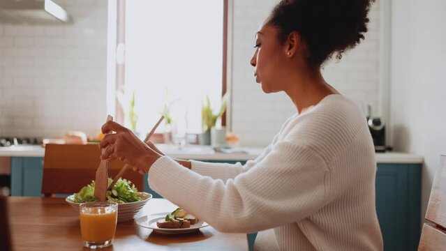 Smiling African pregnant woman tossing salad in the kitchen