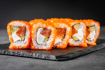 appetizing sushi roll california with salmon cucumber cheese and masago caviar on a black stone...