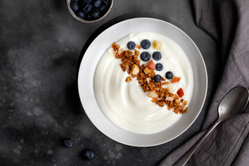 Blueberries in white yogurt with granola in white bowl on grey background. Top view. Breakfast idea.