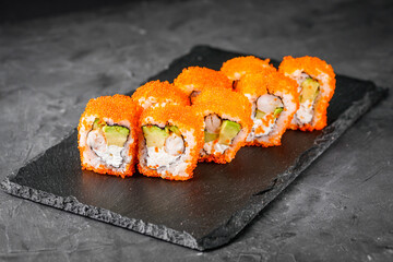 appetizing sushi roll california with avocado shrimp cheese and masago caviar on a black stone plate