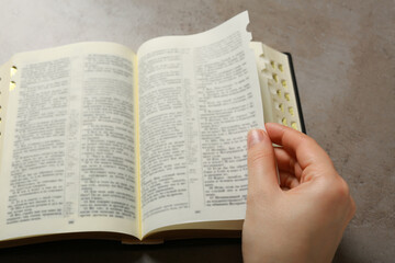 Above view of woman reading Bible at light grey table, closeup