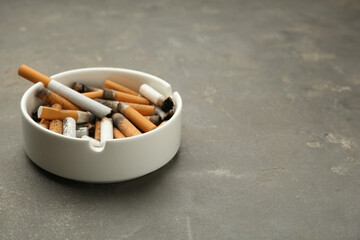 Ceramic ashtray full of cigarette stubs on grey table. Space for text - obrazy, fototapety, plakaty