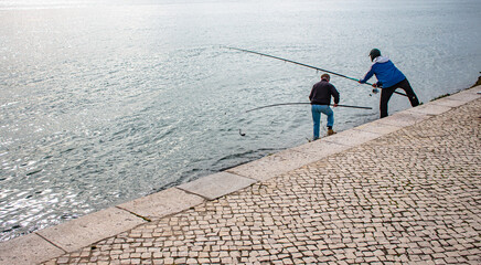 Two anglers catch a fish in a net on a port quay by the river in the glare of the sun. Fishermans....