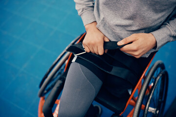 Unrecognizable amputee strapping his legs on wheelchair before sports training.