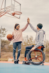 Wheelchair bound athlete and his female friend giving high five after playing basketball outdoors.
