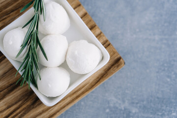Soft Italian white cheese mozzarella on wooden board in white bowl served with fresh rosemary branch