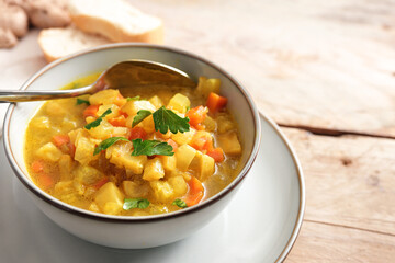 Carrot and celery soup with curry, ginger and parsley garnish in a bowl on a rustic wooden table, vegetarian meal for healthy low carb diet, copy space, selected focus