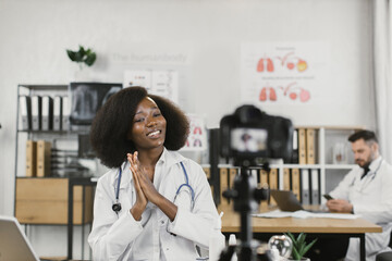 African american woman in lab coat talking and gesturing while recording video blog for her medical channel. Informative blog of competent female doctor.