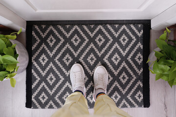 Woman wearing stylish sneakers on door mat in hall, top view
