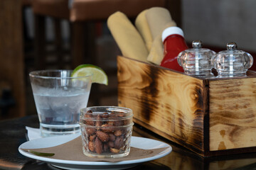 soft focus textured glass jar of almonds with gin and tonic cocktail at a restaurant with wooden box filled with napkins, salt and pepper mills, and ketchup bottle - Powered by Adobe
