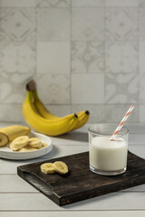 Healthy banana milkshake in a glass and fresh bananas on a wooden board. Delicious vegan drink. Composition with banana smoothies.