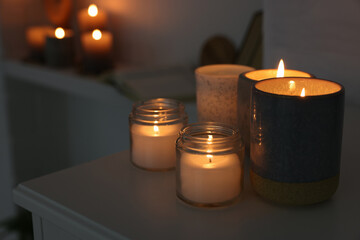 Burning wax candles on white table in room, space for text