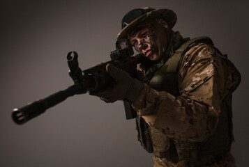 Fototapeta premium Soldier in a military camouflage uniform wearing a helmet, body armor, and holding a machine gun on a gray background. Sniper. Army banner. Military Conflict Actions. Man In Camouflage.