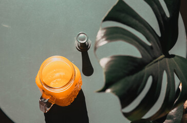 fresh orange juice in summer light and monstera or split-leaf philodendron leaves