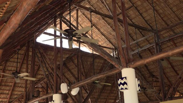 Ceiling fans spinning in a house with a straw roof and a wooden beam in the Caribbean