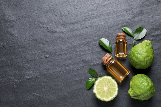 Glass bottles of bergamot essential oil and fresh fruits on black slate table, flat lay. Space for text
