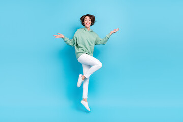 Fototapeta na wymiar Full size photo of impressed millennial brunette lady jump with promo wear hoodie pants sneakers isolated on blue background