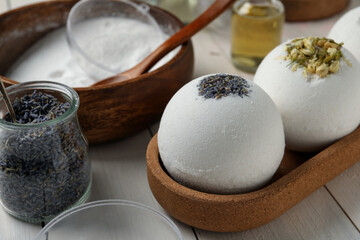 Different bath bombs and ingredients on white wooden table, closeup