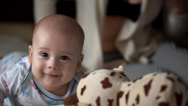Newborn Active Baby With Young Mom. Cute Kid Smiling Teethless Face Portrait Early Days On Stomach Developing Neck Control. Mother And Child Look At Camera Play with Toy. Infant, Beginning Concept
