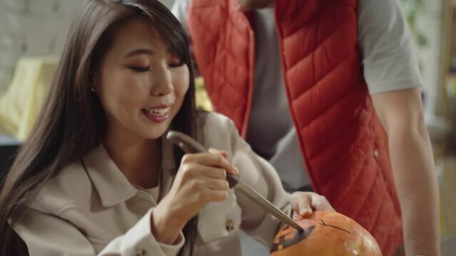 A handsome young lady is carving a mouth of a halloween pumpkin