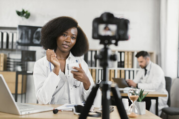 African female practitioner recording video blog about usage of modern infrared thermometer while...
